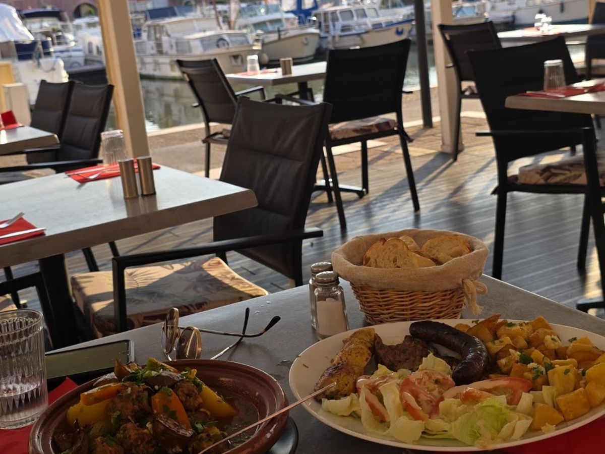 Une table dressée au Cirta, un tajine et une assiette grillade, les bateaux du port en arrière-plan